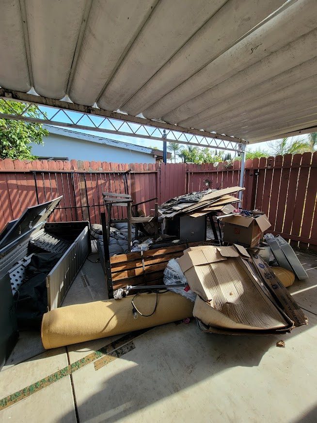 Before: a covered patio filled with old furniture, cardboard and debris during an estate cleanout
